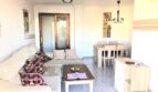Helles Wohnzimmer der Mietwohnung in Cala Ratjada mit Ecksofa, Couchtisch und Essbereich mit Holztisch.
