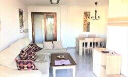 Helles Wohnzimmer der Mietwohnung in Cala Ratjada mit Ecksofa, Couchtisch und Essbereich mit Holztisch.