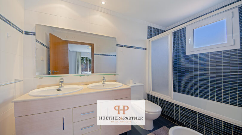 Modernes Badezimmer der Mallorca-Wohnung mit Doppelwaschbecken, blauer Fliesendusche und Badewanne.