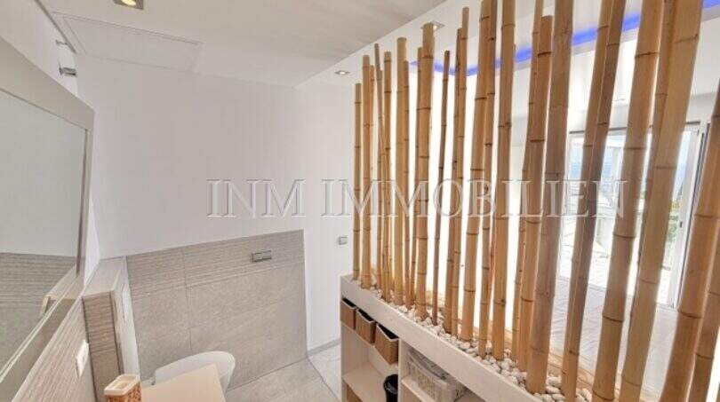 Modernes Badezimmer mit Bambus-Raumteiler, weißer Freistehbadewanne und offenen Regalen im Penthouse Cala Pi