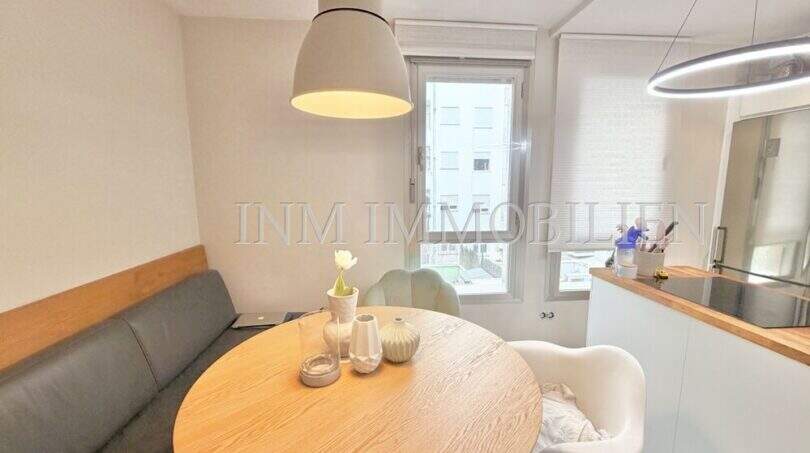 Helle Essecke mit rundem Holztisch, grauer Eckbank und modernen Hängeleuchten in Maisonette-Wohnung, Palma