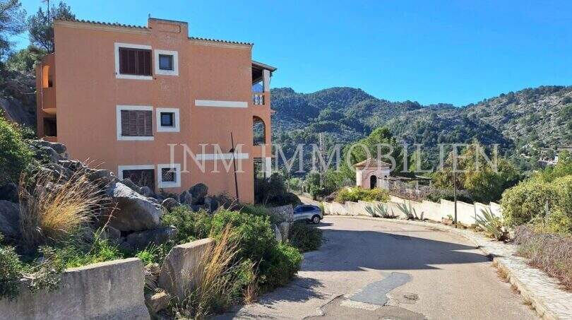 Außenansicht eines mehrstöckigen Wohnhauses in Sóller, umgeben von felsiger Berglandschaft und mediterraner Vegetation.