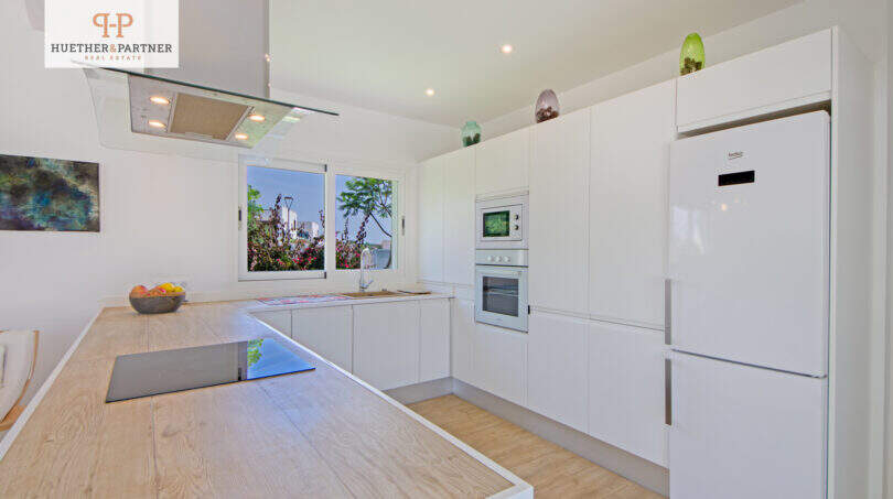 Moderne weiße Einbauküche mit Holzinsel, Beko-Kühlschrank und Gartenblick im EFH Sa Ràpita