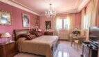 Elegantes Schlafzimmer der Villa in Marratxí mit Kronleuchter, rosa Wänden, Holzbett und klassischen Gemälden.