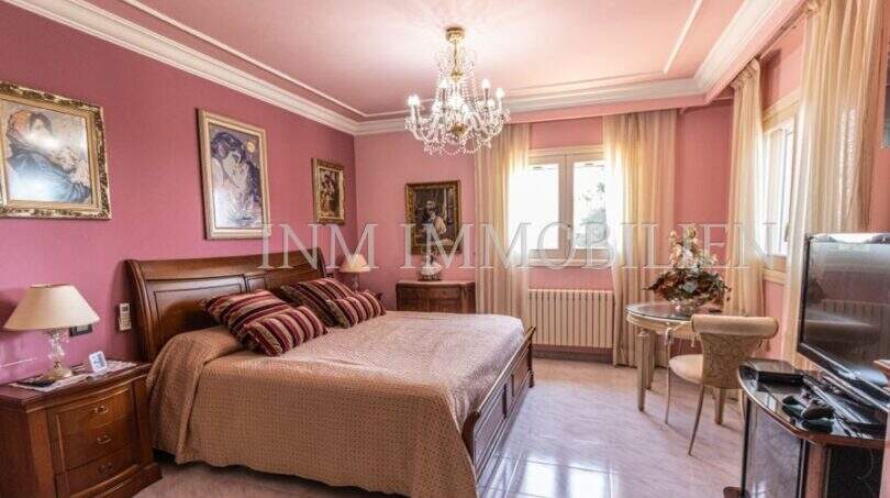 Elegantes Schlafzimmer der Villa in Marratxí mit Kronleuchter, rosa Wänden, Holzbett und klassischen Gemälden.