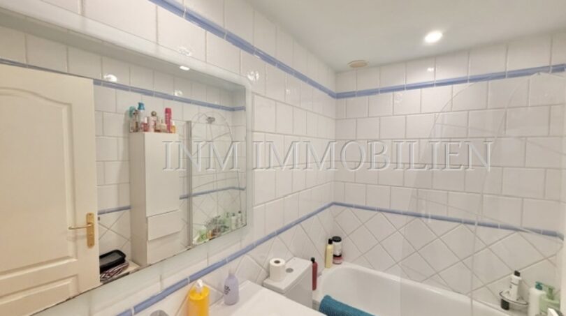 Helles Badezimmer mit weißen Fliesen, blauem Dekorstreifen, Badewanne und Waschtisch im Reiheneckhaus Pollença