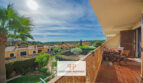 Sonniger Balkon mit Holzmöbeln, Blick über mediterrane Villen und Grünanlagen in Cales de Mallorca