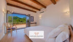 Dormitorio de la finca Felanitx con techo de vigas de madera, cama doble y balcón con vistas a la montaña Sant Salvador