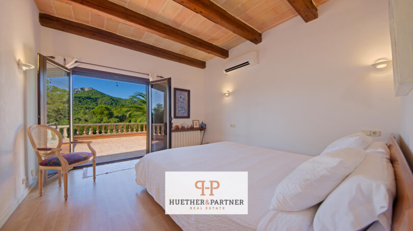 Dormitorio de la finca Felanitx con techo de vigas de madera, cama doble y balcón con vistas a la montaña Sant Salvador