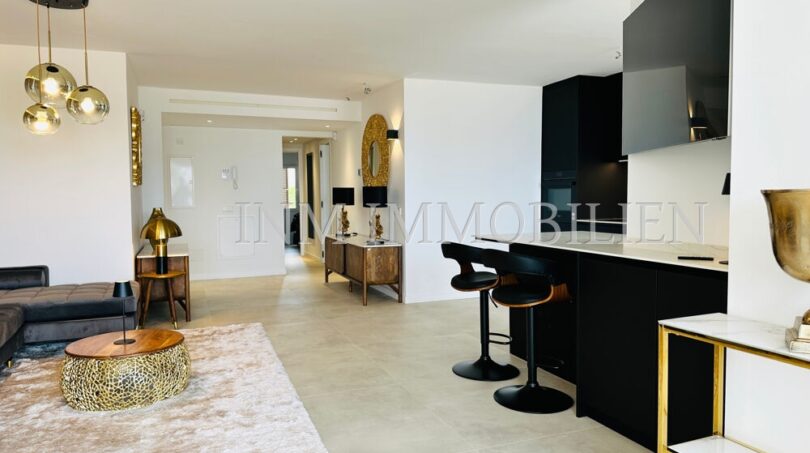 Open living-kitchen area with black designer kitchen, bar stools, gold accents and modern interior in Mallorca designer apartment