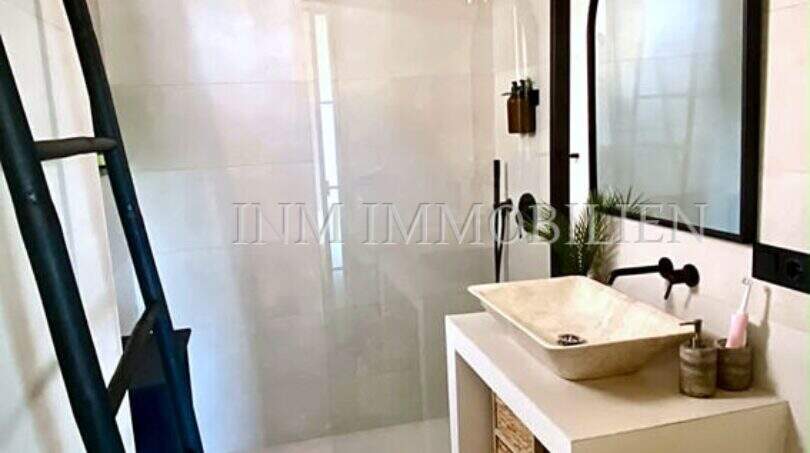 Modernes Badezimmer im Penthouse Playa de Palma mit Regendusche, Naturstein-Waschtisch und schwarzen Designelementen.
