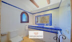 Baño de la finca Felanitx con azulejos azul y blanco, lavabo doble y ventana rústica de arco redondo