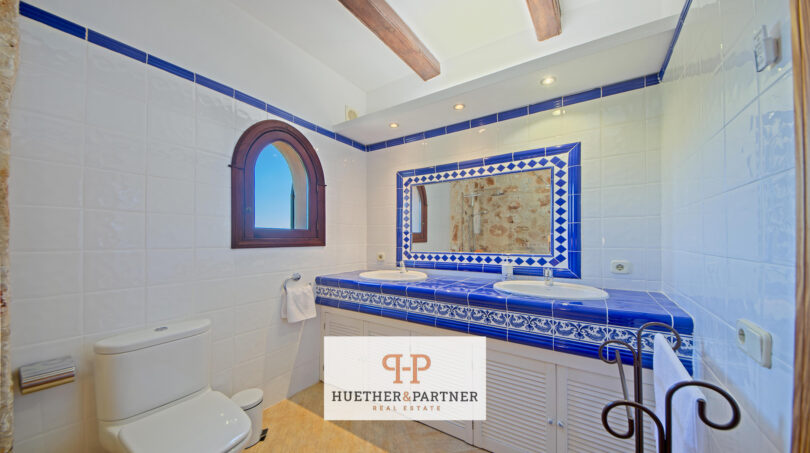 Baño de la finca Felanitx con azulejos azul y blanco, lavabo doble y ventana rústica de arco redondo