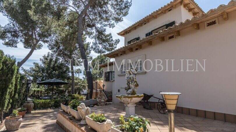 Außenbereich der Villa in Marratxí mit Steinbrunnen, Skulpturen, Terrakottafliesen und mediterranem Garten mit Pinien.