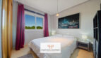 Helles Schlafzimmer der Mallorca-Wohnung mit Doppelbett, roten Vorhängen und Grünblick aus dem Fenster.