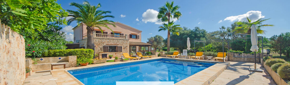Finca Felanitx: Piscina mediterránea con terraza de piedra natural, palmeras y casa de campo rústica bajo cielo azul