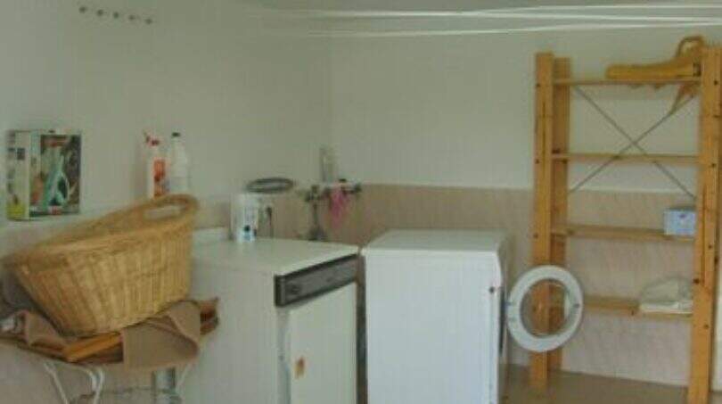 Waschküche mit Waschmaschine, Wäschekorb und Holzregal in der Ferienvilla über der Bucht von Cala Mandia.