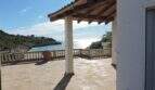 Überdachte Terrasse mit Meerblick auf die Bucht von Cala Mandia, weiße Balustrade, Natursteinboden