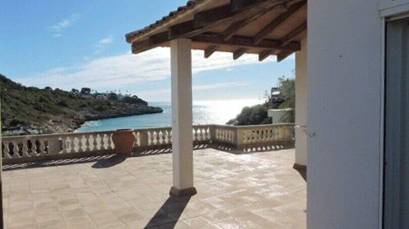 Überdachte Terrasse mit Meerblick auf die Bucht von Cala Mandia, weiße Balustrade, Natursteinboden