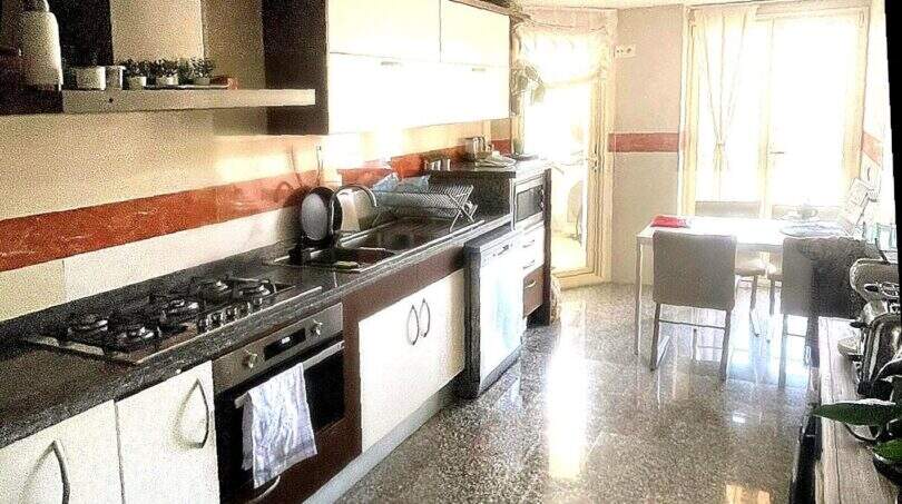 Espaciosa cocina con estufa de gas, horno empotrado, frentes blancos y zona de comedor adyacente con acceso al balcón en Alcudia