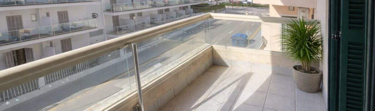 Balcón soleado con barandilla de vidrio y vistas a edificios vecinos en apartamento moderno cerca del mar en Alcudia