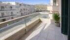 Balcón soleado con barandilla de vidrio y vistas a edificios vecinos en apartamento moderno cerca del mar en Alcudia