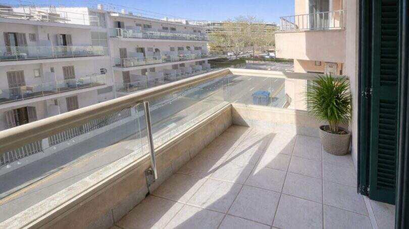 Balcón soleado con barandilla de vidrio y vistas a edificios vecinos en apartamento moderno cerca del mar en Alcudia