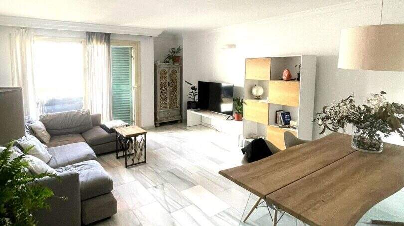 Luminosa sala de estar con sofá gris, mueble TV moderno y mesa de comedor de madera, balcón con vistas al mar en Alcudia