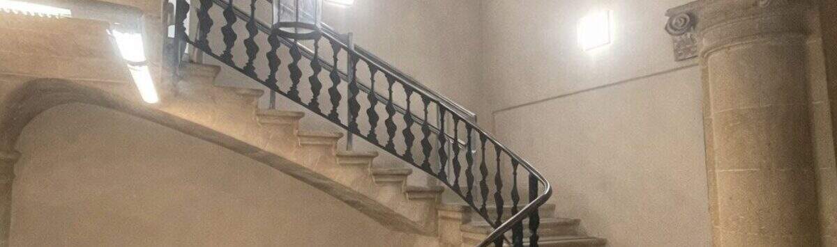 Escalera histórica con escalera de piedra curva, barandilla de hierro forjado y arco abovedado en la casa urbana de Llucmajor
