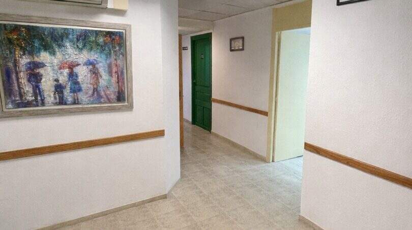 Pasillo luminoso con suelos de baldosa, moldura de madera, cuadro y puerta verde en la casa urbana de Llucmajor