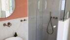 Modernes Badezimmer der Villa mit Glasdusche, Aufsatzwaschbecken, Holzunterschrank und rosafarbener Akzentwand.