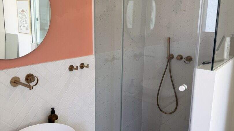 Modernes Badezimmer der Villa mit Glasdusche, Aufsatzwaschbecken, Holzunterschrank und rosafarbener Akzentwand.