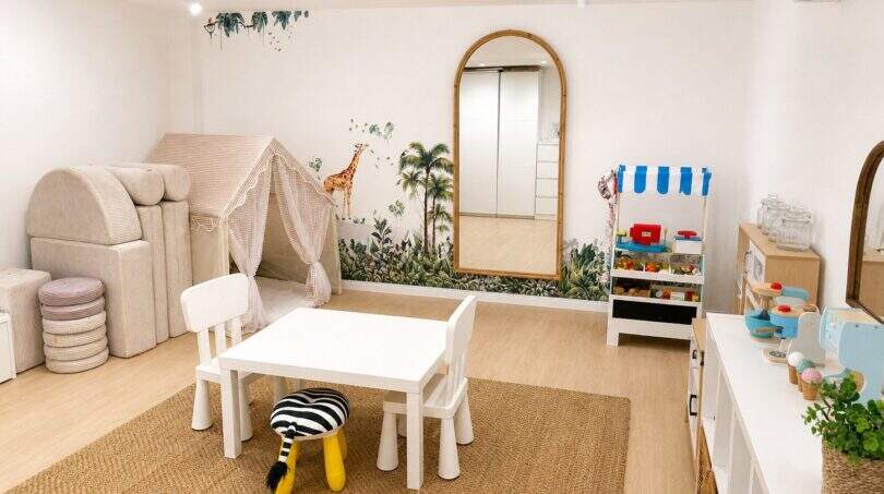 Helles Kinderspielzimmer mit Dschungel-Wandmalerei, Spielküche, Kuschelecke und weißen Möbeln in der Designvilla.