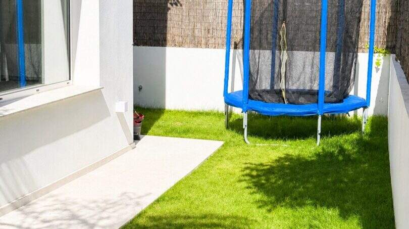 Kleiner Garten der Designvilla in Portixol mit gepflegtem Rasen und blauem Trampolin