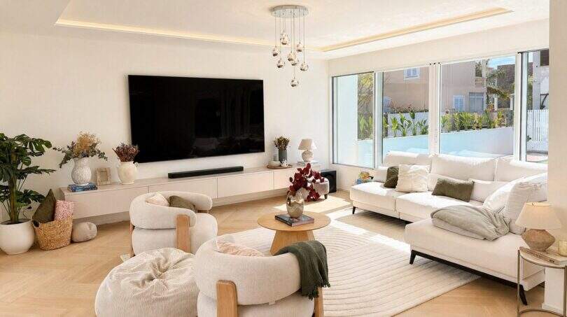 Helles Wohnzimmer der Designvilla in Portixol mit weißen Sofas, Parkettboden und großen Fenstern zum Garten.