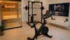 Moderner Fitnessraum mit Peloton-Bike, ATX-Kraftstation, Infrarotsauna und TV-Wandhalterung in exklusiver Villa.