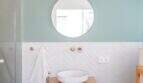 Modernes Badezimmer der Designvilla in Portixol mit Holzwaschtisch, runden Spiegel und mintfarbener Wand.