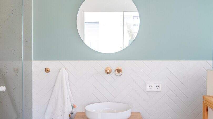 Modernes Badezimmer der Designvilla in Portixol mit Holzwaschtisch, runden Spiegel und mintfarbener Wand.