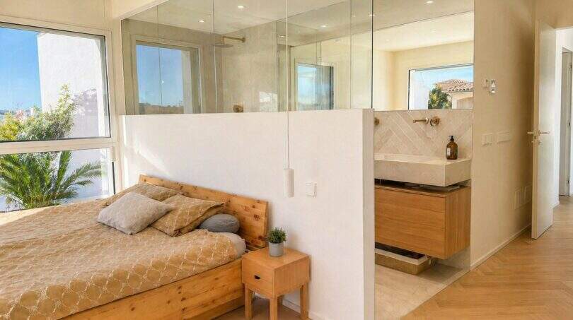Helles Schlafzimmer der Designvilla mit Holzbett, offenem Badbereich und Glastrennwand in Portixol