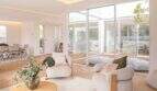 Helles Wohnzimmer der Designvilla in Portixol mit Naturholzboden, modernen Sesseln und Panoramafenstern zum Terrassenbereich.