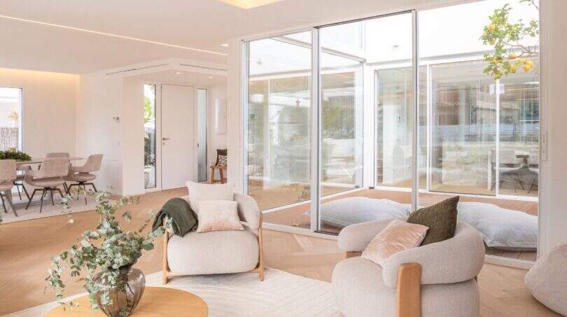 Helles Wohnzimmer der Designvilla in Portixol mit Naturholzboden, modernen Sesseln und Panoramafenstern zum Terrassenbereich.