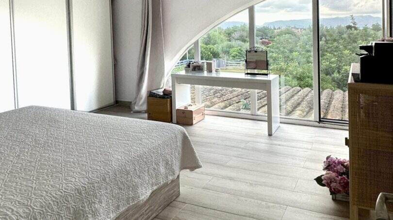 Helles Schlafzimmer der Finca Marratxí mit Bogenfenster, Parkettboden und Blick auf grüne Landschaft.