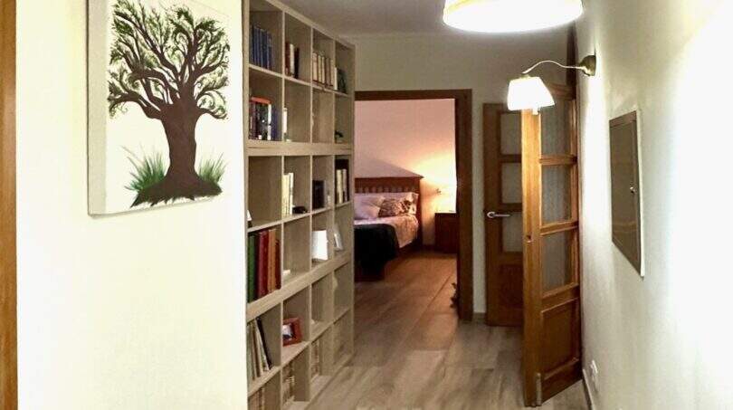 Heller Flur der Finca Marratxí mit Bücherregal, Wandlampen, Holzboden und Blick ins Schlafzimmer