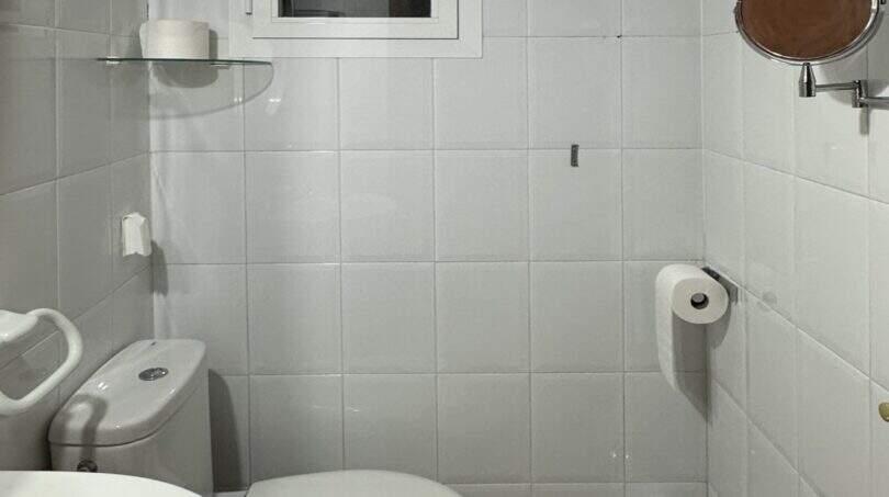 Helles Badezimmer der Mallorca-Finca mit weißen Fliesen, WC, Waschbecken und Wandspiegel