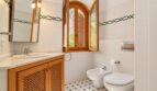 Helles Badezimmer der Finca mit Bidet, WC, Holzunterschrank und Bogenfenster mit Gartenblick.