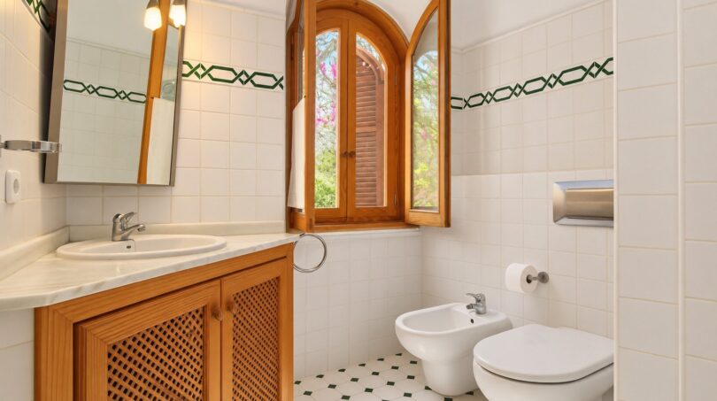 Helles Badezimmer der Finca mit Bidet, WC, Holzunterschrank und Bogenfenster mit Gartenblick.