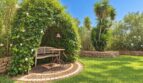 Gepflegter Garten der Natursteinfinca mit Sitzecke, Rankpflanzen-Pavillon und mediterranen Palmen.