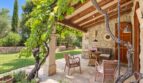 Überdachte Terrasse der Natursteinfinca mit Rattanmöbeln, Weinrebe und gepflegtem Garten