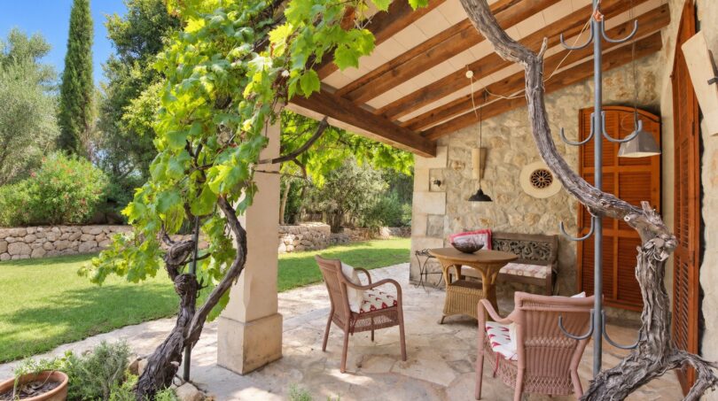 Überdachte Terrasse der Natursteinfinca mit Rattanmöbeln, Weinrebe und gepflegtem Garten