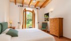 Helles Schlafzimmer der Natursteinfinca mit Holzbalkendecke, Doppelbett und Blick in den Garten.
